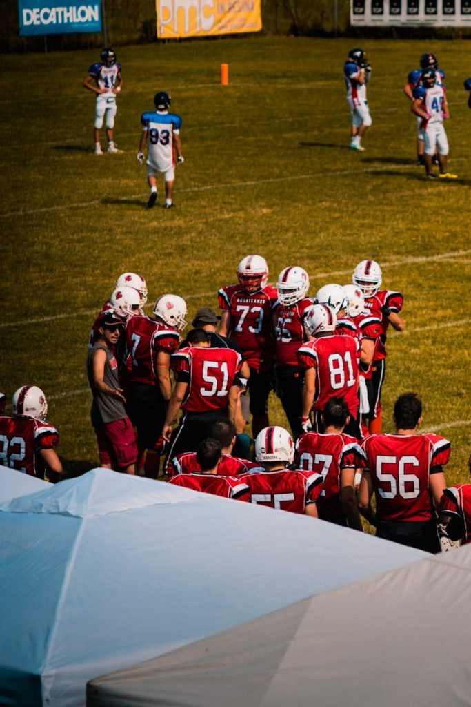 Group of American football players strategizing on a sunny day at a sports field.