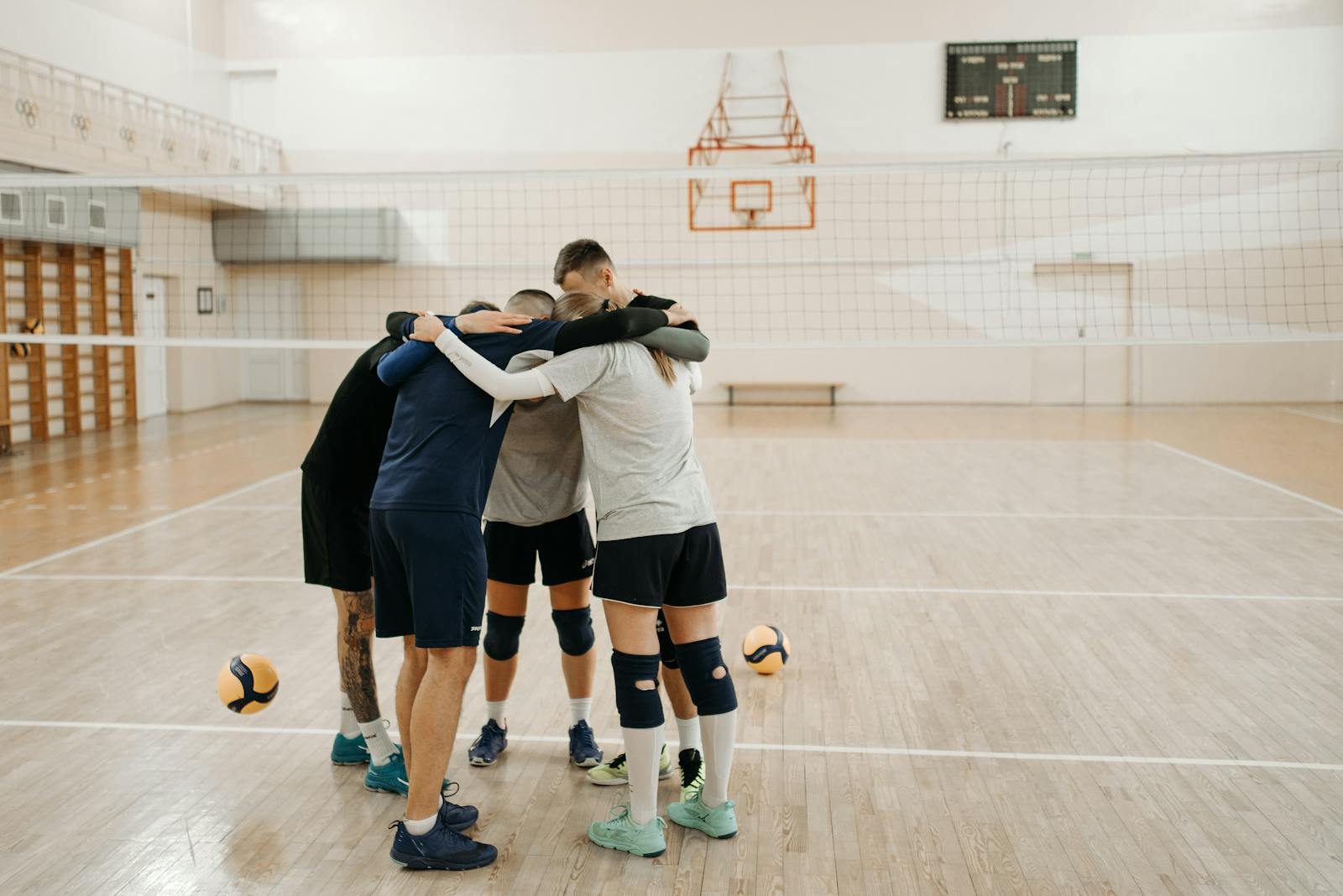 Team of young adults huddling on an indoor volleyball court, fostering teamwork and unity.